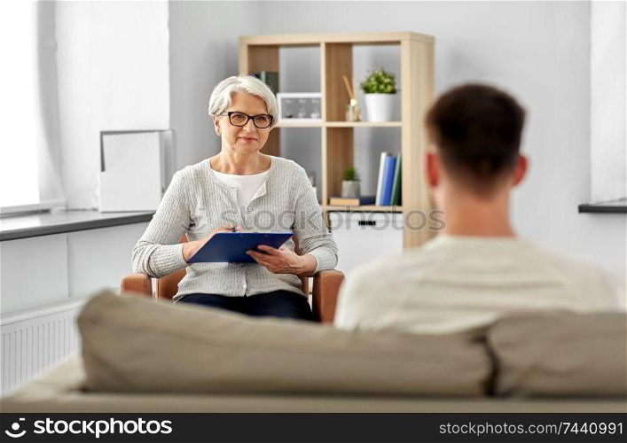 psychology, mental therapy and people concept - senior woman psychologist with clipboard and young man patient at psychotherapy session. senior woman psychologist and young man patient