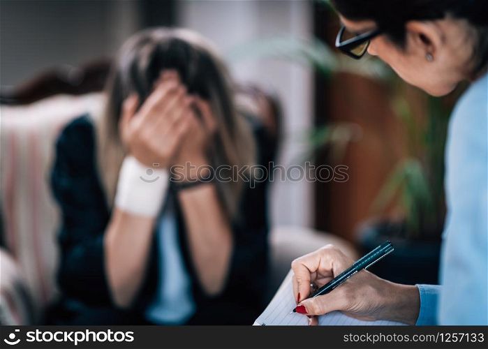 Psychotherapist taking notes during CBT session with mental health patient.