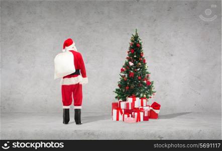 ptesents, holidays and people concept - man in costume of santa claus with bag over concrete wall and christmas tree background