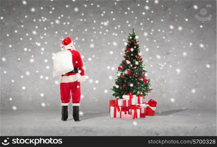 ptesents, holidays and people concept - man in costume of santa claus with bag over concrete wall, snowflakes and christmas tree background