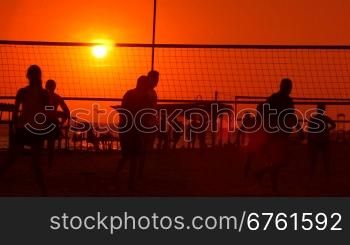 Public beach with a volleyball courts and players silhouettes in the sun city on horizon
