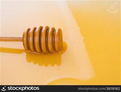 puddle of honey with wooden stick as background
