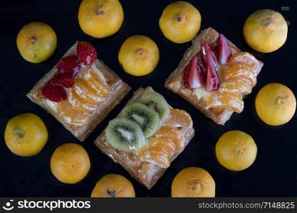 puff pastry with tangerine, kiwi and strawberry fruit on black background