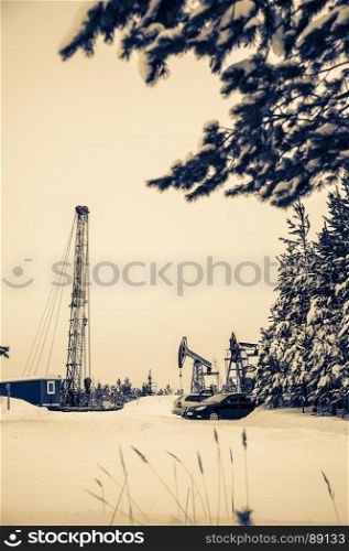 Pump jack and oil rig in the oilfield situated in the beautiful winter forest. Environmental pollution. Oil and gas concept. . Pump jack and oil rig situated in forest.