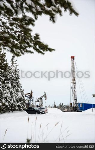 Pump jack and oil rig situated in forest.. Pump jack and oil rig in the oilfield situated in the beautiful winter forest. Environmental pollution. Oil and gas concept.