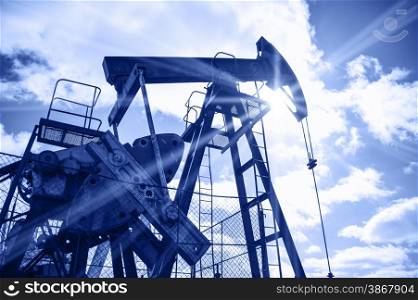 Pump jack on a sky and sun background. Extraction of oil. Toned blue.. Oil rig.