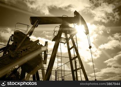 Pump jack on a sky and sun background. Extraction of oil. Toned sepia.. Oil rig.