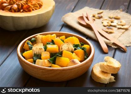 Pumpkin and chard salad with croutons served in wooden bowl, photographed on dark wood with natural light (Selective Focus, Focus in the middle of the salad)