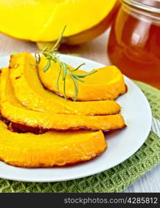 Pumpkin baked with honey in a bowl on a napkin, a jar of honey, raw pumpkin on a lighter background of wooden boards