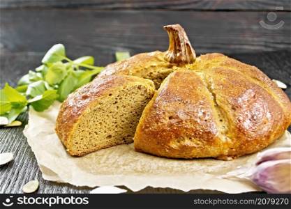 Pumpkin bread cut on parchment, garlic, basil and seeds on the background of a dark wooden board