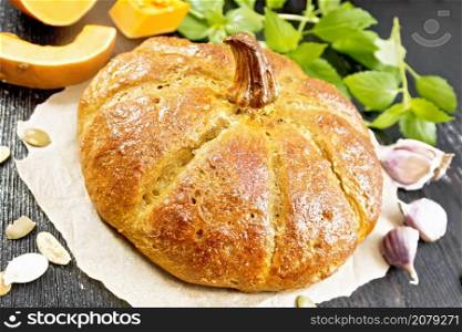 Pumpkin bread on paper, garlic, basil, pieces and seeds of a vegetable on a black wooden board background