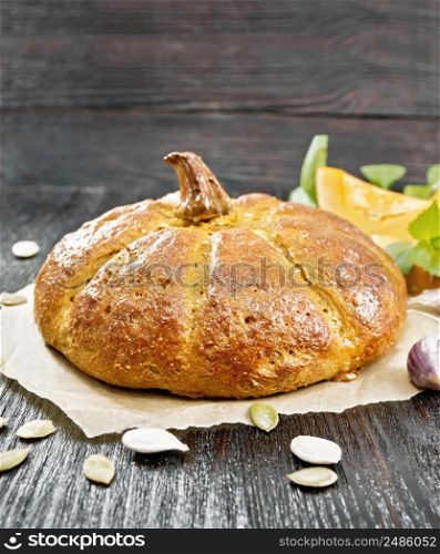 Pumpkin bread on paper, garlic, basil, pieces and seeds of a vegetable on a wooden board background