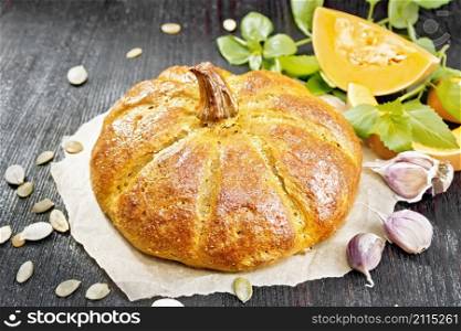 Pumpkin bread on parchment, garlic, basil, pieces and seeds of a vegetable on a wooden board background