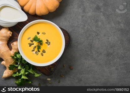 Pumpkin carrot vegetarian soup with parsley, olive oil and pumpkin seeds in a white bowl, top view. Layout on gray background with ingredients, copy space for menu