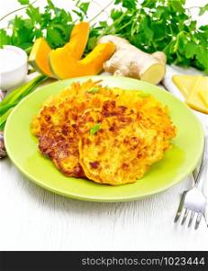 Pumpkin, cheese and ginger fritters in a green plate, sour cream in a bowl, napkin, parsley and fork on background of light wooden board