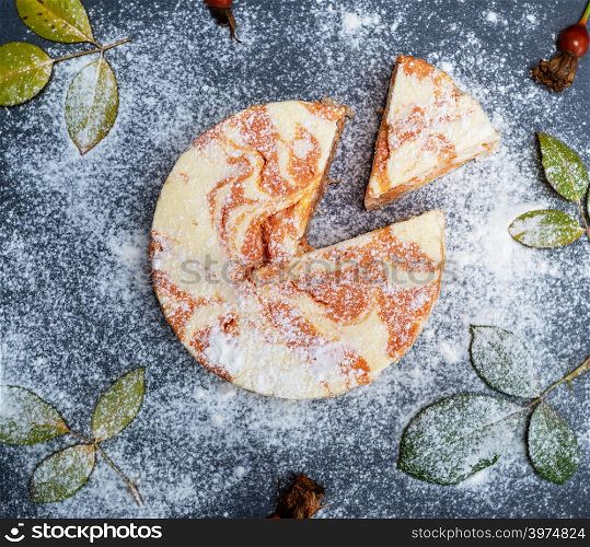 pumpkin cheesecake sprinkled with powdered sugar on a black background, top view