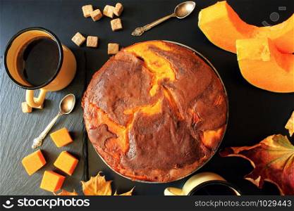Pumpkin chocolate cake on dark background with fall leaves, top view .