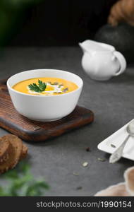 Pumpkin chowder with cream, pumpkin seeds and parsley in a white bowl on a gray background. Seasonal vegetarian soup, selective focus on parsley