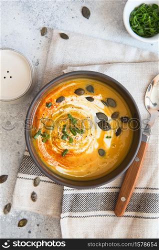 Pumpkin cream soup. Roasted pumpkin and carrot puree soup with turmeric, cream, paprica, chives and pumpkin seeds on grey background. Vegetarian cousine. Vegan recipe. Green living. Organic food.