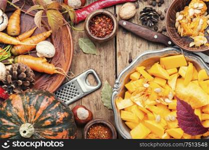 Pumpkin cut in a pieces and food ingredients.Autumn vegetarian food on wooden background. Pumpkin and ingredients for cooking