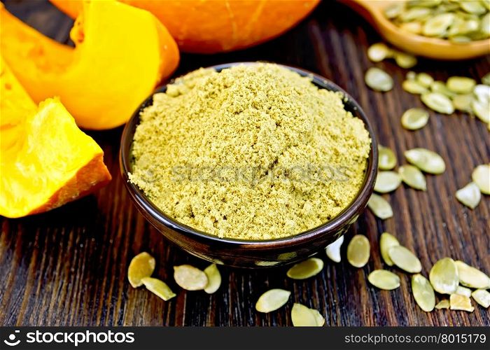 Pumpkin flour in a bowl, peeled pumpkin seeds in a spoon on the table, slices of fresh pumpkin on a wooden boards background