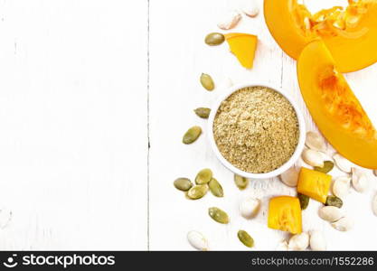 Pumpkin flour in a bowl, seeds on the table, slices of vegetable on wooden board background from above