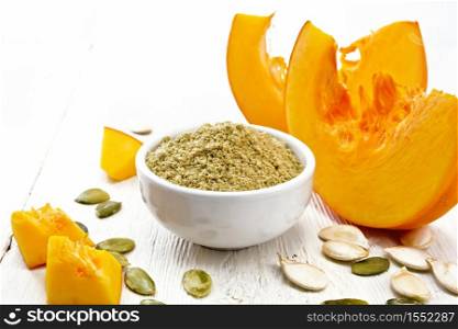 Pumpkin flour in a bowl, seeds on the table, slices of vegetable on a wooden board background