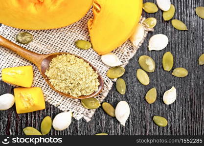 Pumpkin flour in a spoon on burlap, seeds and pieces of vegetable on wooden board background from above