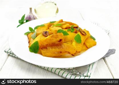 Pumpkin fried with garlic, cinnamon and vinegar in a plate on a towel, oil and mint on background of white wooden board
