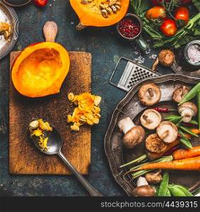 Pumpkin half on cutting board with spoon , mushrooms and vegetables ingredients for tasty vegetarian cooking, top view