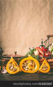Pumpkin halves on kitchen table with cooking pot and ingredients at rustic wall background, front view. Healthy vegetarian food and eating concept. Autumn seasonal eating