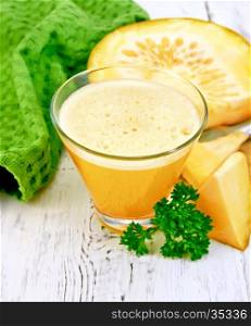 Pumpkin juice in a tall glass with pieces of pumpkin, parsley and a napkin on a wooden boards background