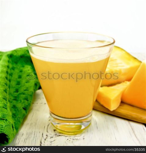 Pumpkin juice in a tall glass with slices of pumpkin, napkin on background wooden plank