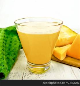Pumpkin juice in a tall glass with slices of pumpkin, napkin on background wooden plank