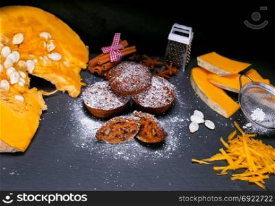 pumpkin muffins and pieces of fresh pumpkin on a black background, top view