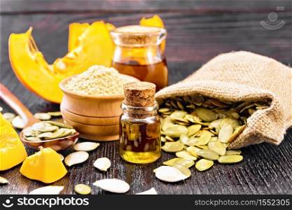 Pumpkin oil in vial and a jar, flour in a bowl, seeds in a spoon and bag, slices of vegetable on black wooden board background