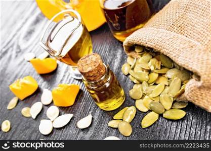 Pumpkin oil in vial, gravy boat and a jar, seeds in a bag and on table, slices of vegetable on wooden board background