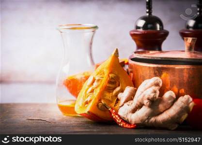 Pumpkin on kitchen desk table with cooking pot, oil and ginger. Food background for Autumn cooking inspiration and Recipes
