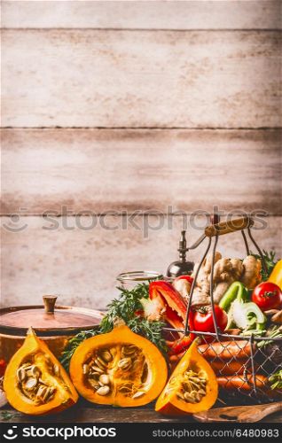 Pumpkin on kitchen table with cooking pot and ingredients at rustic wall background, front view. Healthy vegetarian food and eating concept. Autumn seasonal eating