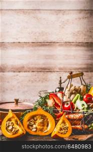 Pumpkin on kitchen table with cooking pot and ingredients at rustic wall background, front view. Healthy vegetarian food and eating concept. Autumn seasonal eating