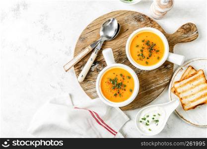 pumpkin or carrot or sweet potato vegetable soup in white bowls served on a light background, top view, space for a text