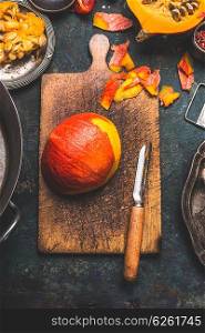 Pumpkin peeling on rustic cutting board with vegetables peeler , dark wooden background, top view