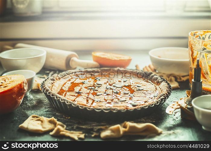 Pumpkin pie on kitchen table at window with cooking ingredients