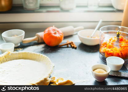 Pumpkin pie preparation on kitchen table at window with cooking ingredients