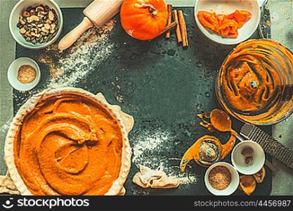 Pumpkin pie preparation with ingredients and kitchen tools on dark rustic background, top view, frame. Thanksgiving day food concept