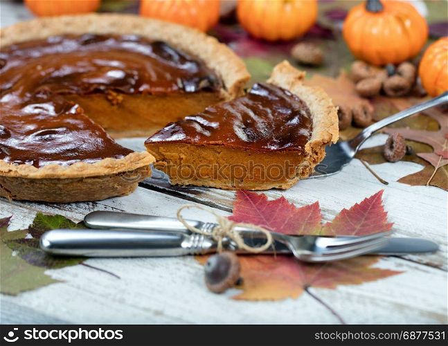 Pumpkin pie with autumn foliage and small pumpkins in background. Thanksgiving holiday concept.