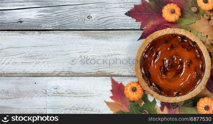 Pumpkin pie with autumn foliage and small pumpkins on rustic white wood. Thanksgiving holiday concept in flat lay format.