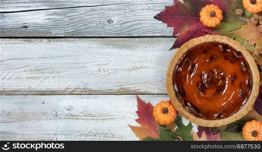 Pumpkin pie with autumn foliage and small pumpkins on rustic white wood. Thanksgiving holiday concept in flat lay format.