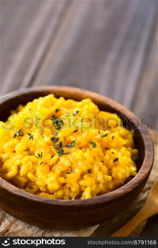 Pumpkin risotto prepared with pumpkin puree and sprinkled with fresh thyme leaves served in wooden bowl, photographed with natural light (Selective Focus, Focus one third into the risotto)