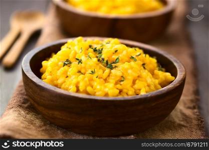 Pumpkin risotto prepared with pumpkin puree and sprinkled with fresh thyme leaves served in wooden bowls, photographed with natural light (Selective Focus, Focus one third into the risotto)